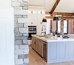 A kitchen with stone walls and white cabinets.