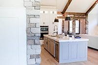 A kitchen with stone walls and white cabinets.